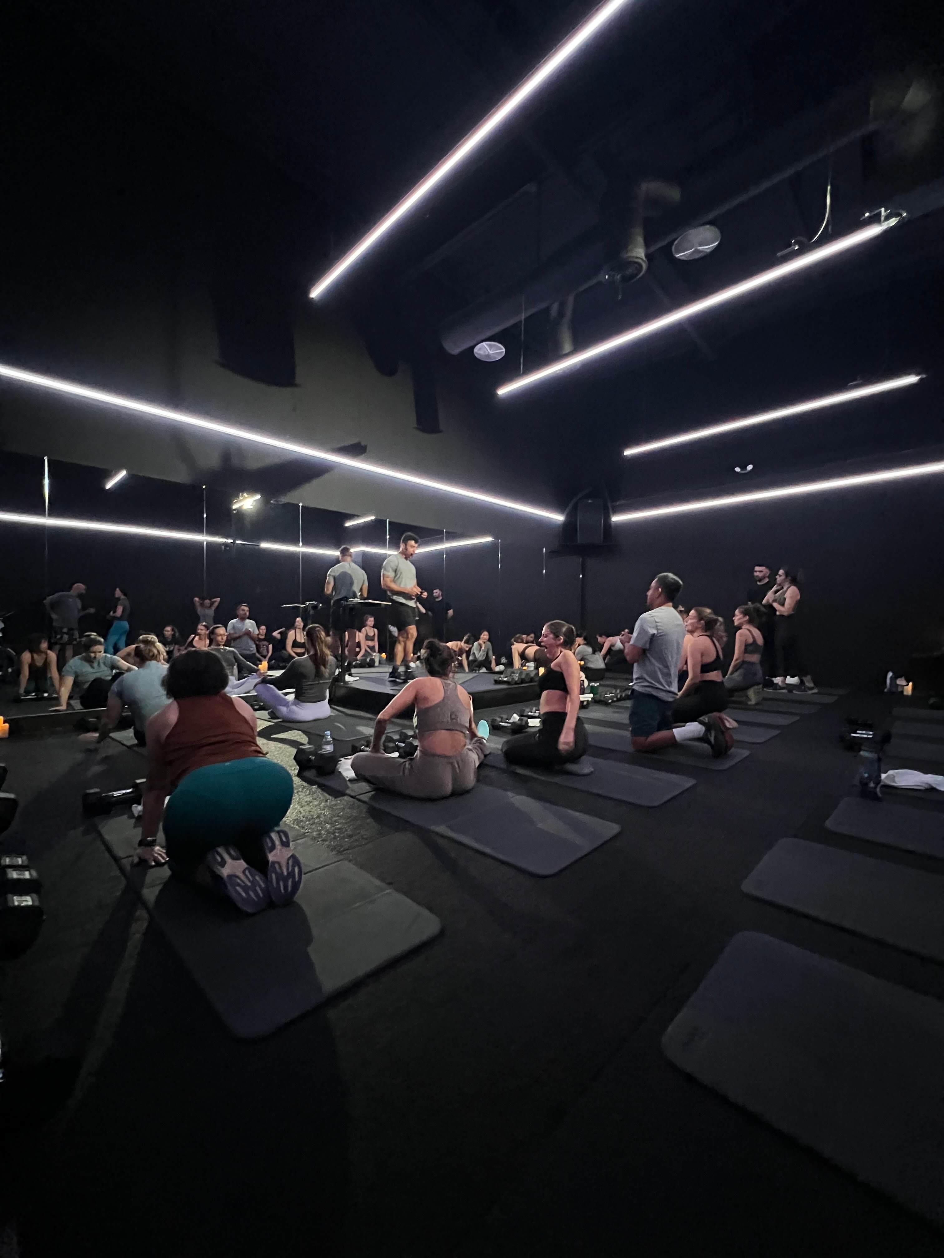 Group class on mats under geometric neon overhead lighting — Ceremny dark studio