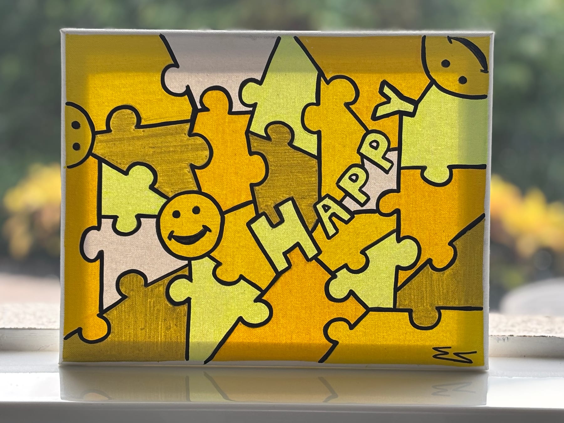 A small canvas painting of interlocking yellow jigsaw pieces, with the word HAPPY lettered across several of the pieces and smiling faces among them.